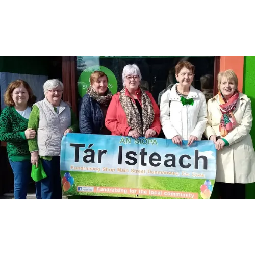 Image of volunteers of the Tar Isteach Fundraising shop in Dunmanway holding up a banner with the Shops name