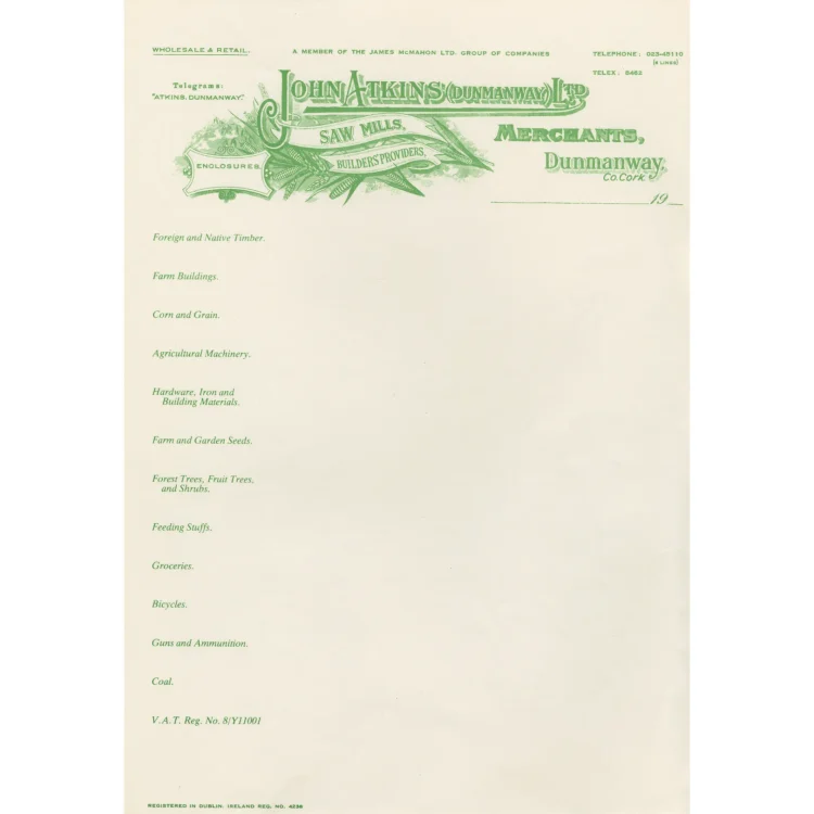 A vintage cream-coloured business letterhead for "John Atkins (Dunmanway) Ltd". At the top, a detailed green graphic logo depicts a farming scene with wheat stalks framing banners that read "Saw Mills" and "Builders Providers". The text identifies them as "Merchants, Dunmanway, Co. Cork". The left side lists wholesale and retail goods in green text, including timber, farm buildings, agricultural machinery, seeds, groceries, and bicycles.